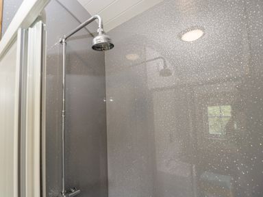 A shower area with a wall-mounted showerhead and reflective speckled wall panels at Ridgeway in Uffington