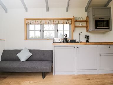 A kitchen area with gray cabinets and wooden countertop next to a gray sofa with a blue cushion at Ridgeway in Uffington