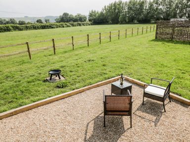An outdoor seating area with two chairs and a table on gravel next to a grassy field with a fire pit at Ridgeway in Uffington