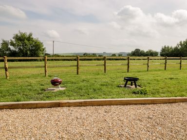 A grassy outdoor area with two barbecue grills and a wooden fence at Ridgeway in Uffington