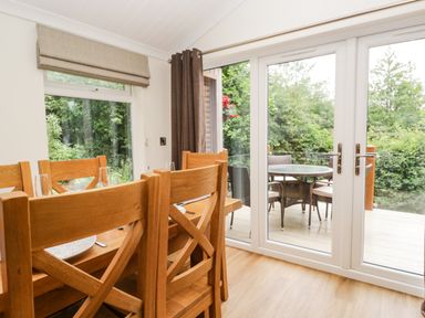 A dining area with wooden chairs and table near glass doors opening to an outdoor patio with a round table and chairs at Robin Lodge in Cartmel