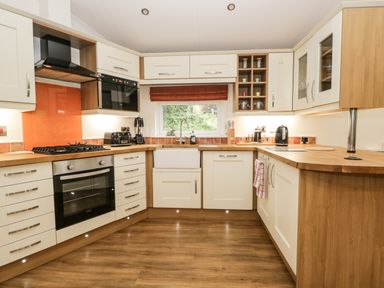 A kitchen with white cabinets wooden countertops a black oven and stove and a window with a red blind at Robin Lodge in Cartmel