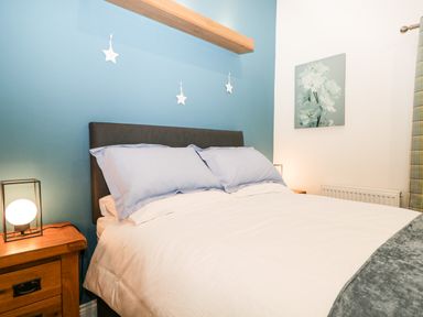 A bedroom with a double bed, bedside tables with lamps, blue accent wall, and a floral painting at Robin Lodge in Cartmel