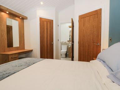 A bedroom with a bed a wooden dressing table and a view of a bathroom through an open door at Robin Lodge in Cartmel