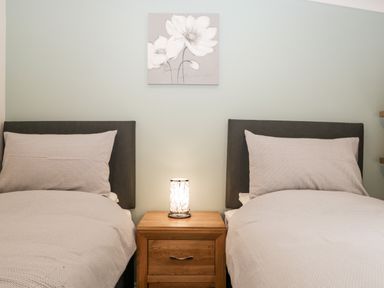 A bedroom with two single beds separated by a wooden nightstand with a lamp and a floral painting on the wall at Robin Lodge in Cartmel