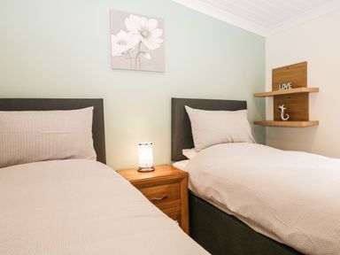 A bedroom with two single beds a wooden nightstand with a lamp and floating shelves on the wall at Robin Lodge in Cartmel