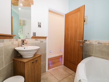 A bathroom with a wooden door a white sink on a wooden cabinet and a white bathtub with a towel at Robin Lodge in Cartmel