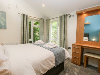 A bedroom with a bed, plaid curtains, a wooden dressing table with a mirror and a stool at Robin Lodge in Cartmel