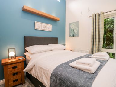 A bedroom with a double bed bedside tables lamps and a window with plaid curtains at Robin Lodge in Cartmel