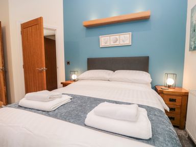A bedroom with a double bed white towels on the bed wooden bedside tables and blue accent wall at Robin Lodge in Cartmel