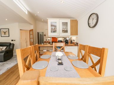 A dining table with six chairs and plates in a kitchen and living area at Robin Lodge in Cartmel