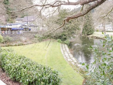 A riverside with grass and stone steps near buildings and trees at Dolwen in Penmachno