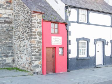 The smallest house in great britain with a red facade and wooden door between stone and white buildings