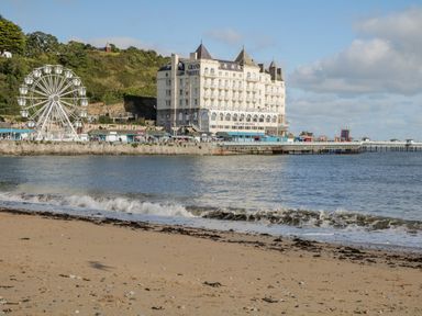 A sandy beach in front of a large white Grand Hotel near a Ferris wheel and pier at Dolwen in Penmachno