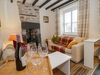 A living room with a stone fireplace a bottle of wine and wine glasses on a tray at Dolwen in Penmachno