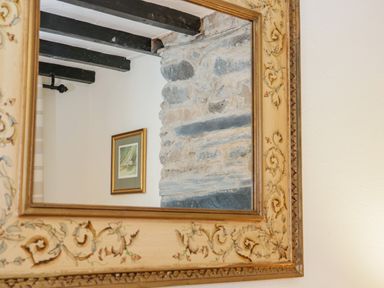 A mirror reflecting a stone wall with black wooden beams and a framed picture at Dolwen Penmachno