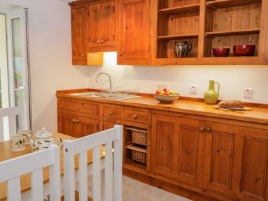A kitchen with wooden cabinets a sink a bowl of fruit a loaf of bread and a table with chairs at Dolwen in Penmachno