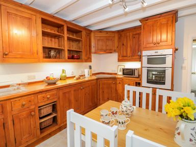 A kitchen with wooden cabinets a dining table with mugs and a vase of flowers at Dolwen in Penmachno