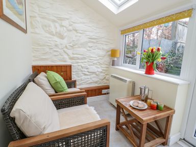 A seating area with wooden framed wicker chairs a wooden side table with cups and a plate near a window with a vase of flowers at Dolwen in Penmachno