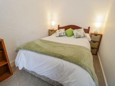 A bedroom with a double bed with green and white pillows and two bedside tables with lamps at Dolwen in Penmachno