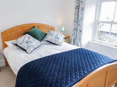 A bedroom with a wooden bed frame blue quilt and floral pillows at Dolwen in Penmachno
