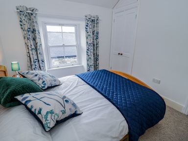 A bedroom with a bed covered in white sheets and blue bedding next to a window with floral curtains at Dolwen in Penmachno