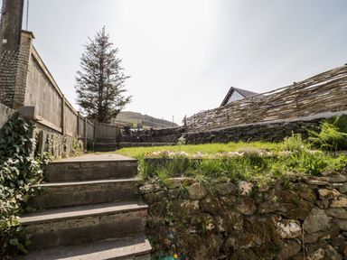 A garden area with stone steps leading to a patio with chairs and a table at Dolwen in Penmachno