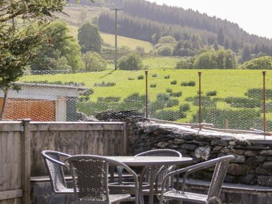 An outdoor table with four metal chairs on a patio overlooking a green field and trees at Dolwen in Penmachno