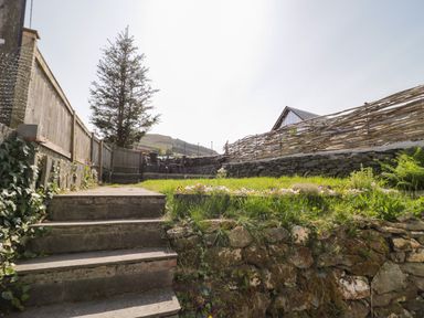 A garden with stone steps leading to a grassy area with a table and chairs behind a wooden fence at Dolwen in Penmachno