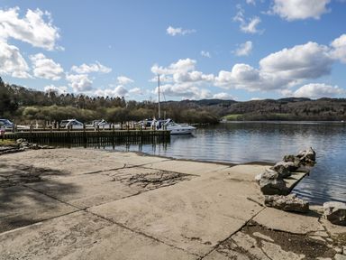 A boat dock with several boats moored and a cracked concrete ramp leading to the water at Grizedale Lodge Langdale 18 White Cross Bay near Windermere