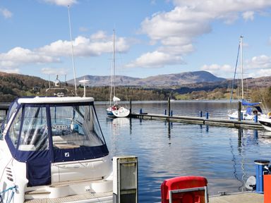 A marina with boats docked on a lake with hills and blue sky in the background at Grizedale Lodge in Langdale 18 White Cross Bay near Windermere