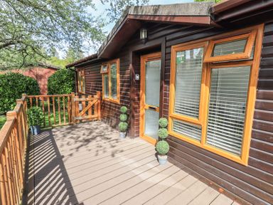 A wooden deck outside a cabin with potted plants and a wooden gate at Grizedale Lodge Langdale 18 White Cross Bay near Windermere