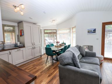 An open plan room with a kitchen area sink and cabinets a dining table with green chairs and a gray sofa at Grizedale Lodge Langdale 18 White Cross Bay near Windermere