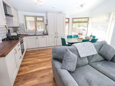 An open kitchen and dining area with white cabinets wooden countertops a grey sofa and green dining chairs at Grizedale Lodge Langdale 18 White Cross Bay near Windermere
