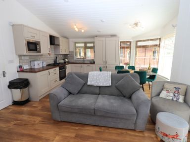 A kitchen and dining area with a grey sofa and armchair in the foreground at Grizedale Lodge Langdale 18 White Cross Bay near Windermere