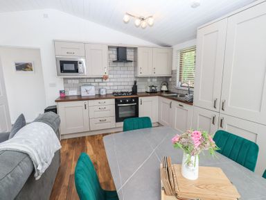 A kitchen and dining area with beige cabinets green chairs and a table with a flower vase at Grizedale Lodge in Langdale 18 White Cross Bay near Windermere