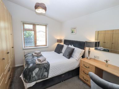 A bedroom with a double bed beside a window and wooden wardrobes at Grizedale Lodge Langdale 18 White Cross Bay near Windermere