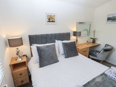 A bedroom with a bed and gray pillows two bedside tables with lamps and a wooden desk with a chair at Grizedale Lodge Langdale 18 White Cross Bay near Windermere