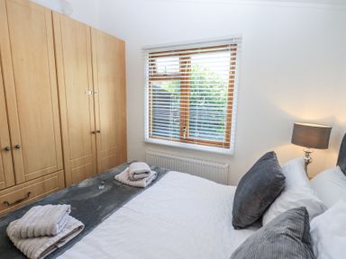 A bedroom with a bed with gray pillows and folded towels next to a wooden wardrobe and a window with blinds at Grizedale Lodge Langdale 18 White Cross Bay near Windermere