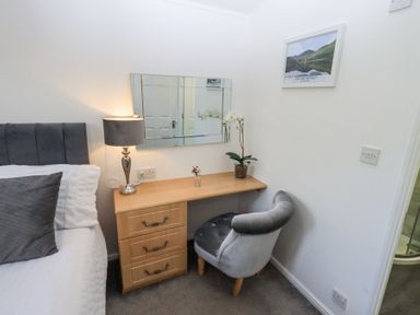A bedroom corner with a wooden desk and gray chair next to a bed and a picture on the wall at Grizedale Lodge in Langdale 18 White Cross Bay near Windermere