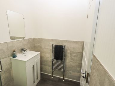 A small bathroom with a sink and cabinet a wall mirror a towel rack with a towel and a door at Grizedale Lodge Langdale 18 White Cross Bay near Windermere