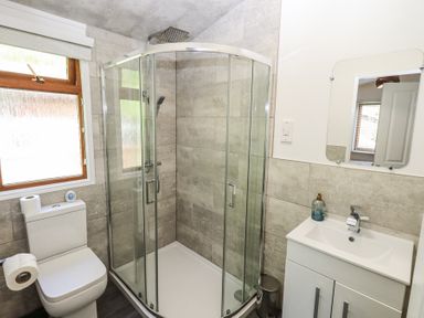 A bathroom with a toilet, glass shower enclosure, sink with faucet, mirror, window, and soap dispenser at Grizedale Lodge Langdale 18 White Cross Bay near Windermere