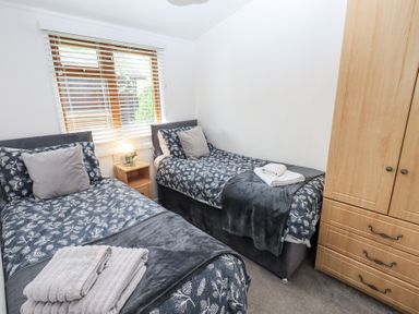 A bedroom with two single beds a wooden wardrobe and a window with blinds at Grizedale Lodge Langdale 18 White Cross Bay near Windermere