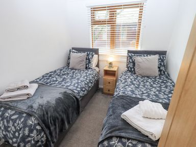 A bedroom with two single beds a small wooden nightstand and a window with blinds at Grizedale Lodge Langdale 18 White Cross Bay near Windermere