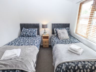 A bedroom with two single beds with patterned bedding and a nightstand with a lamp between the beds at Grizedale Lodge Langdale 18 White Cross Bay near Windermere