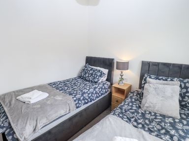 A bedroom with two single beds blue patterned bedding a wooden bedside table and a lamp at Grizedale Lodge Langdale 18 White Cross Bay near Windermere