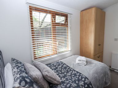 A bedroom with a bed with patterned bedding and folded towels next to a wooden wardrobe at Grizedale Lodge Langdale 18 White Cross Bay near Windermere