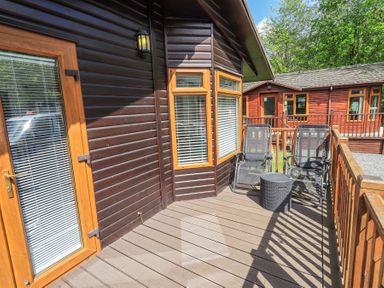 A wooden deck with two black mesh chairs and a small round table outside wooden cabins at Grizedale Lodge Langdale 18 White Cross Bay near Windermere