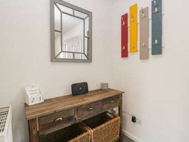 A hallway with a wooden console table baskets mirror and colorful coat hooks at 26 Hycemoor Way Bootle Near Millom