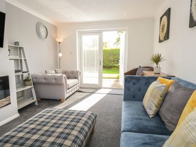 A living room with sofas a plaid ottoman and glass doors leading to a garden at 26 Hycemoor Way Bootle Near Millom